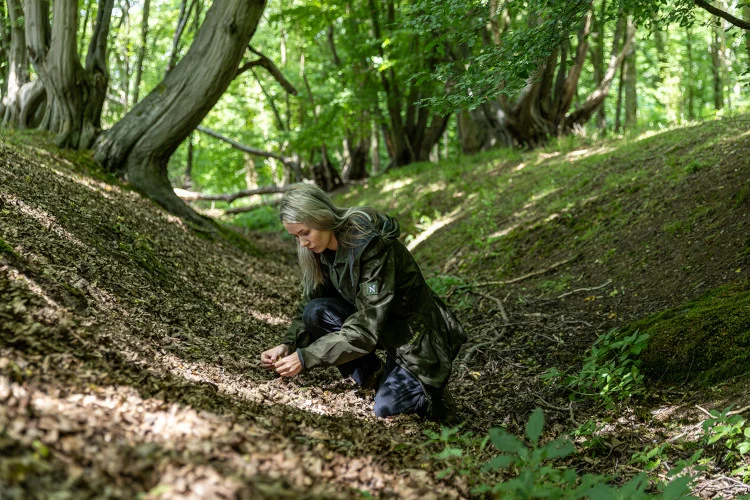 A woman looking closely at what she has found underneath the trees in a wood